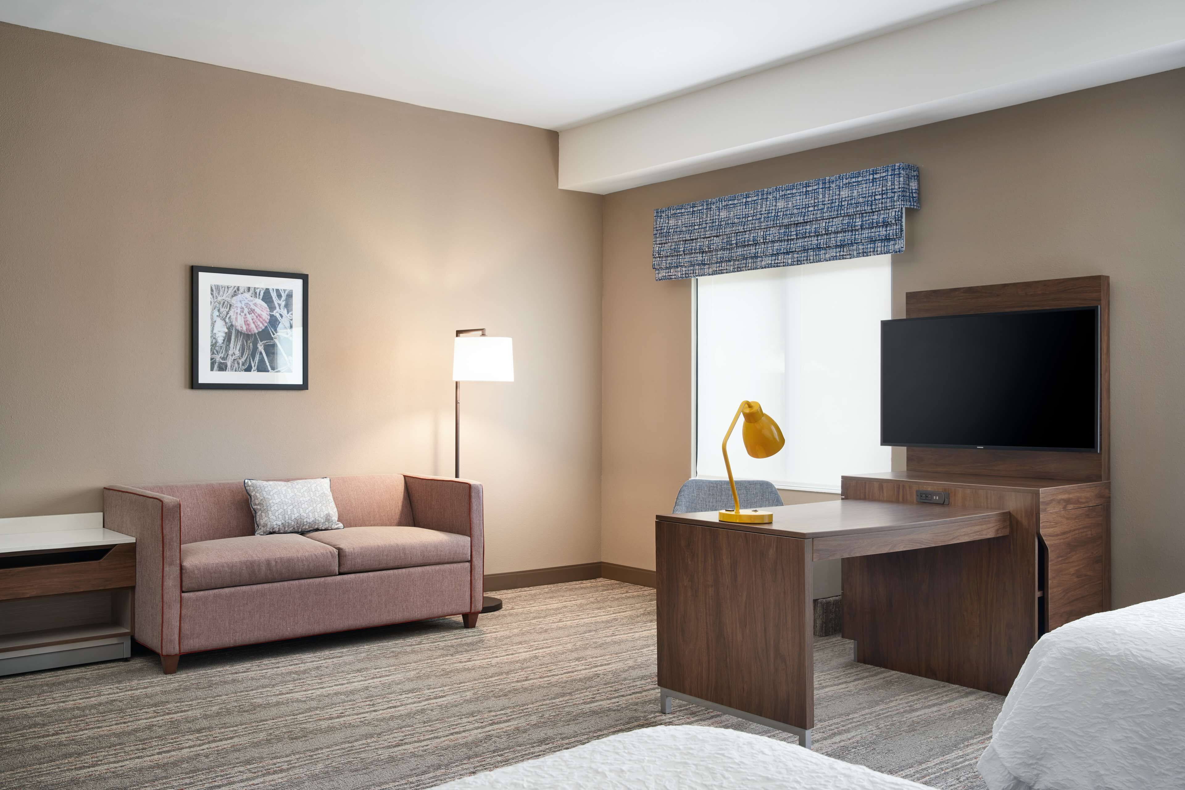 Habitación de hotel con sofá, escritorio, televisor de pantalla plana y un cuadro en la pared.