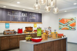 Una barra de desayuno con un menú en pizarra, un frutero y un dispensador de jugo.