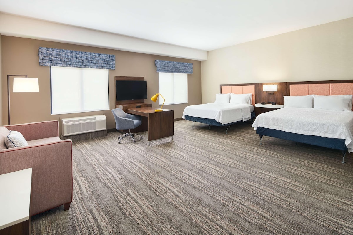 Ein Hotelzimmer mit zwei Betten, einem Schreibtisch, einem Stuhl, einem Fernseher und einem Schlafsofa.
