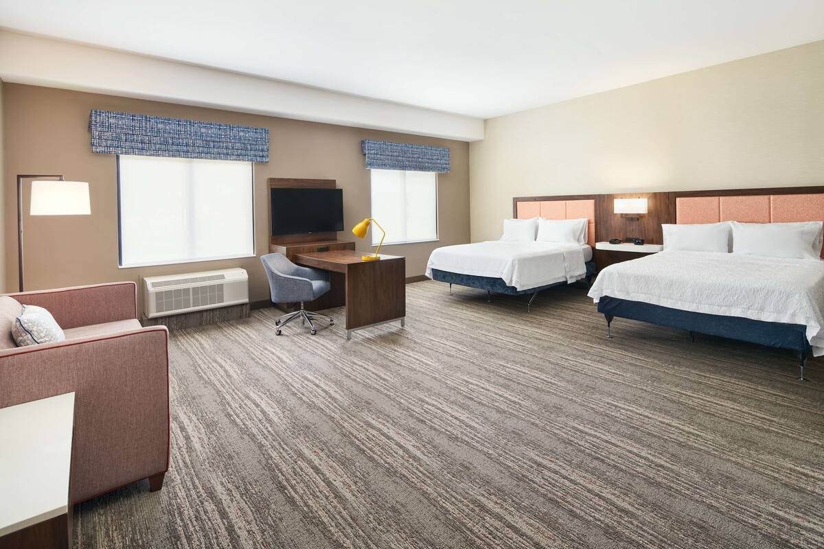 Ein Hotelzimmer mit zwei Betten, einem Schreibtisch, einem Stuhl, einem Fernseher und einem Sofa.