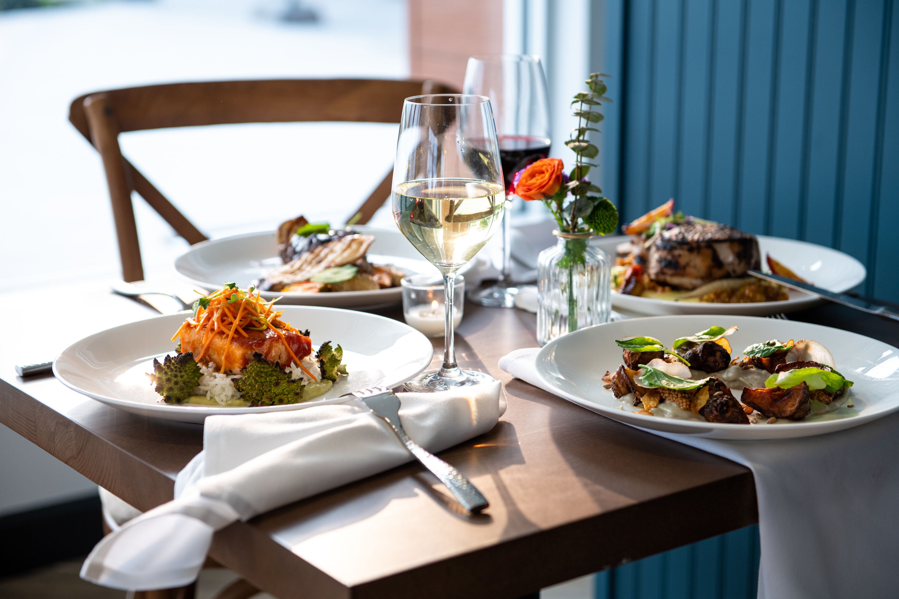 A dining table with plates of food, a wine glass, and a vase with a flower.