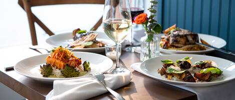 A dining table with plates of food, a wine glass, and a vase with a flower.