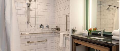 Een moderne badkamer met witte metro betegeling, een glazen douchecabine, een wastafel met donker aanrechtblad en een grote spiegel.