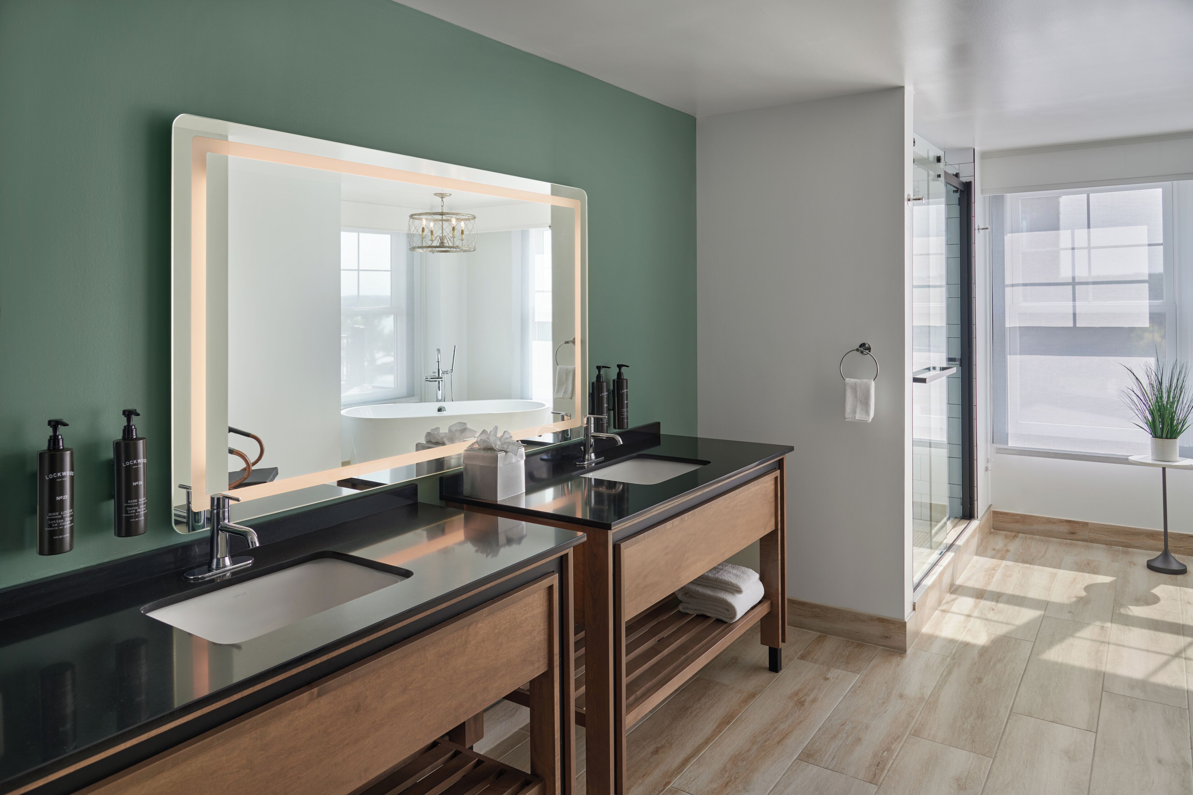 A modern bathroom with two sinks, a large mirror, and a potted plant.