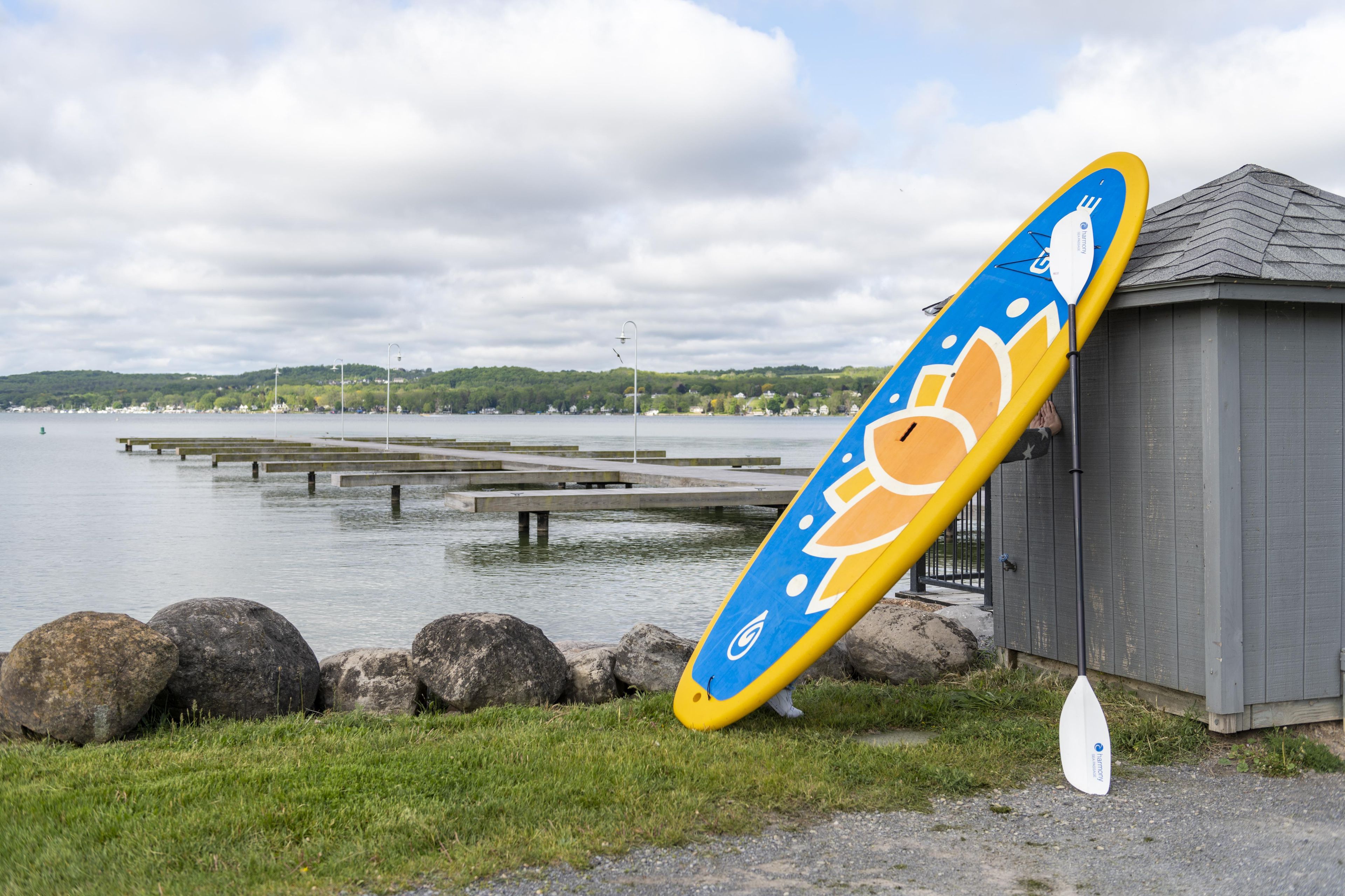 A kayak leaning against a building by a lake with a dock in the background.