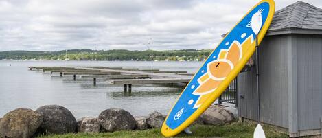 A kayak leaning against a building by a lake with a dock in the background.