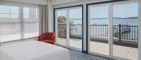 Habitación de hotel con una cama grande, una silla roja y vistas al agua a través de amplios ventanales correderas.