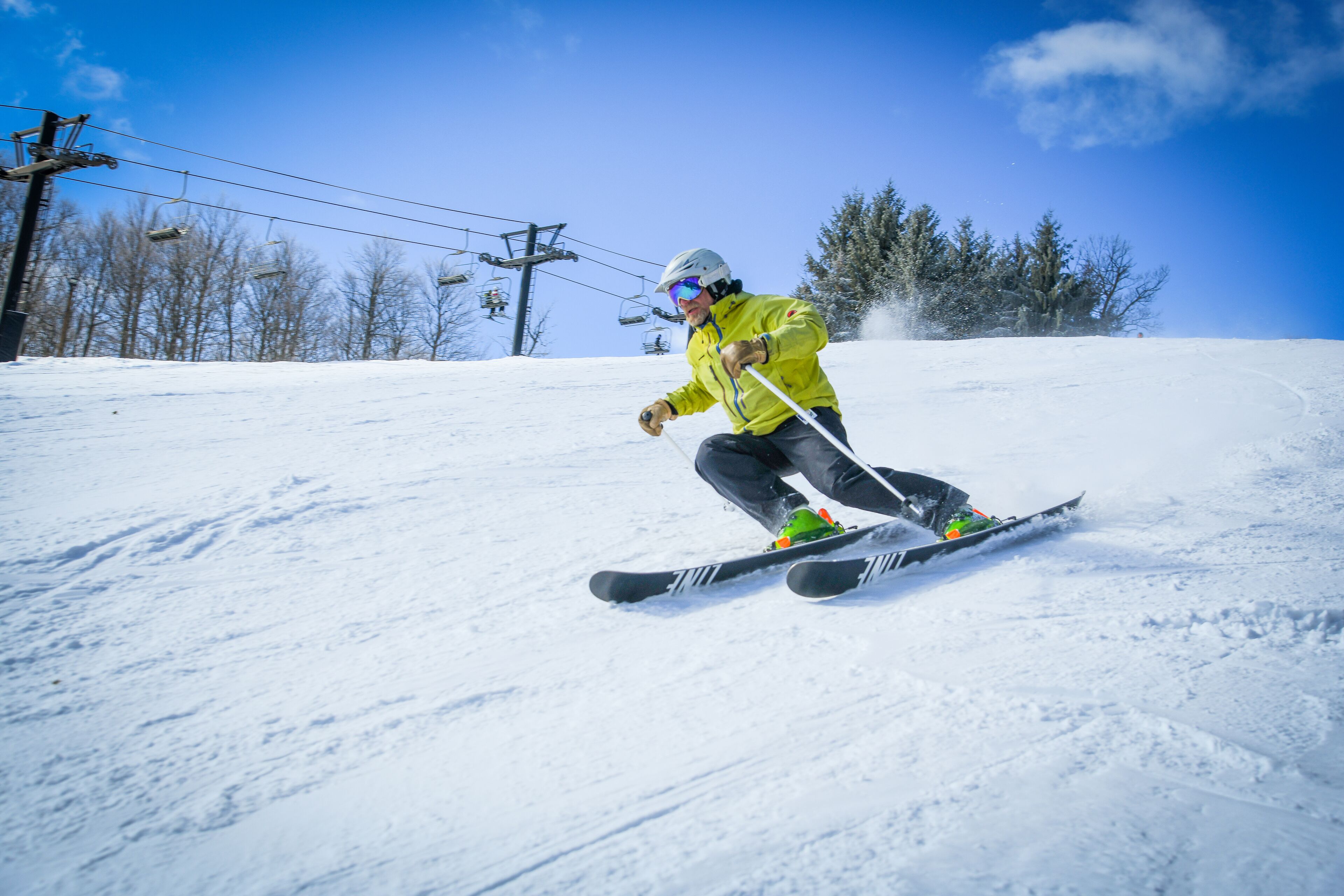 A person skiing on a snowy slope with ski lifts in the background.