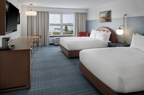 A hotel room with two beds, a desk, a TV, and a large window with a view of a body of water. - Hotel Canandaigua, Tapestry Collection by Hilton (Canandaigua)