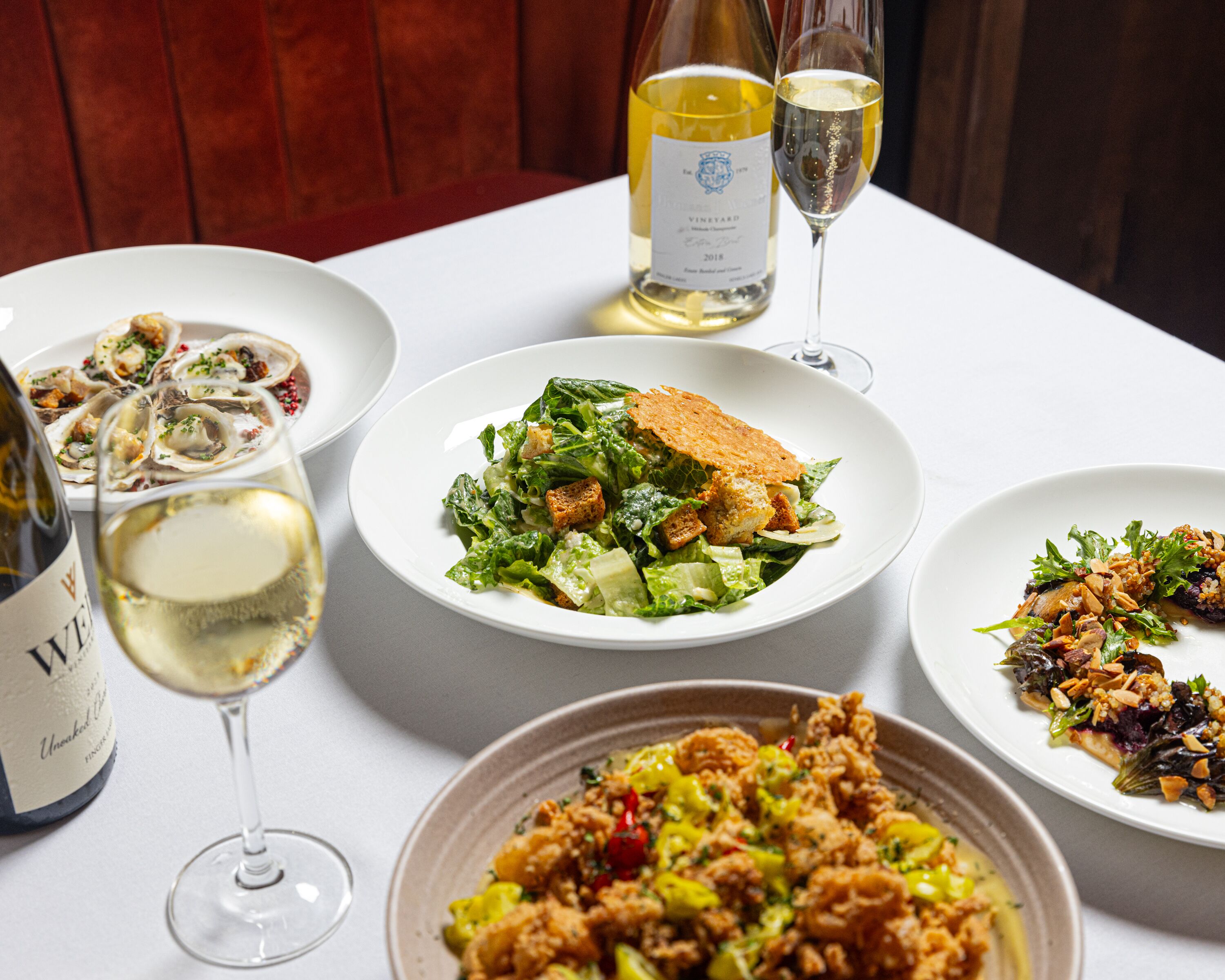 Una mesa de comedor con varios platos y copas de vino blanco.