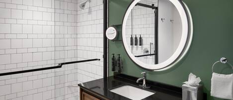 A modern bathroom with a black countertop, a round mirror, and a glass shower enclosure.