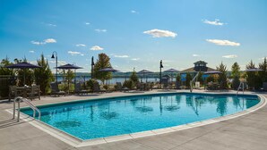 Piscina con sillas de descanso y sombrillas, rodeada por una valla y árboles.
