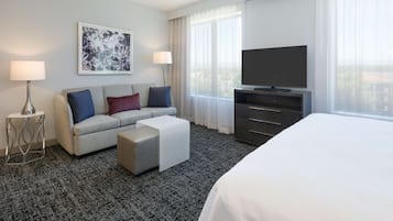 A hotel room with a bed, a sofa, a TV, a desk, and a window with curtains.