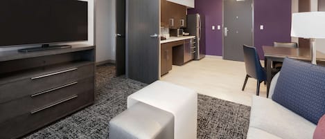 Una sala de estar moderna con un televisor de pantalla plana, un sofá, una mesa de centro y una kitchenette al fondo.
