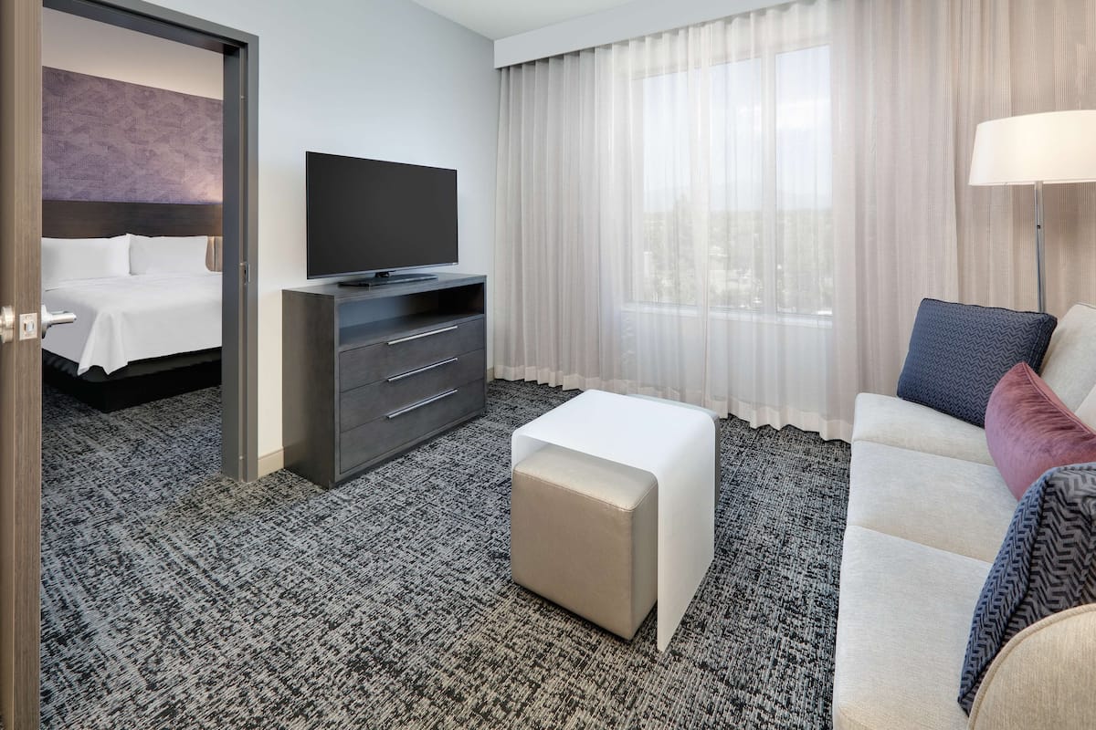 Une chambre d’hôtel avec un lit, une télévision, un canapé, une table basse et une fenêtre avec des rideaux.