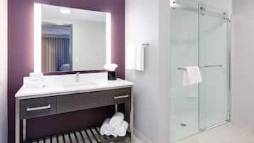 Un baño moderno con un espejo grande, lavabo blanco, tocador oscuro y mampara de vidrio.