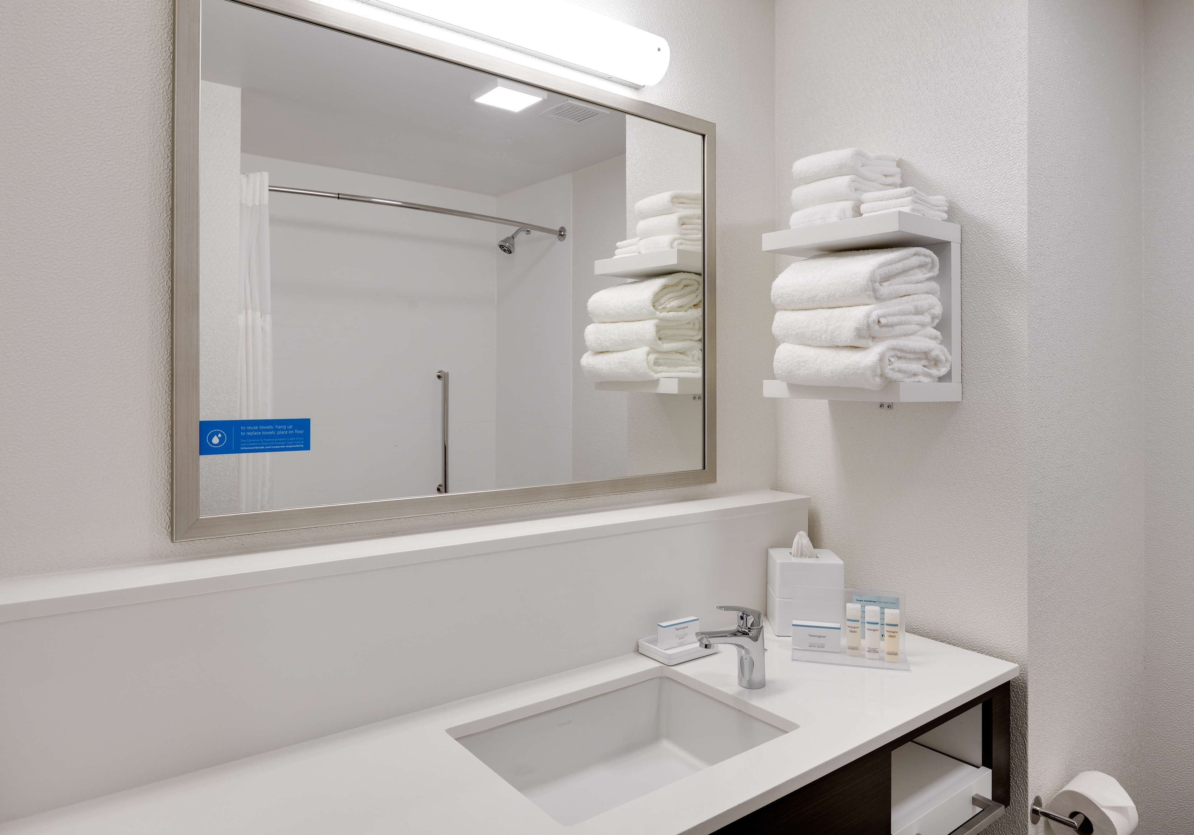 A modern bathroom with a large mirror, a white sink, and neatly folded towels on a shelf.