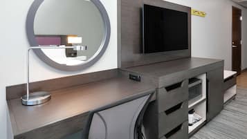 Una habitación de hotel moderna con un escritorio de madera, un espejo grande, un televisor de pantalla plana y cajones integrados.