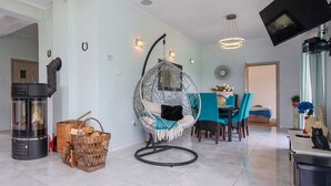 Una sala de estar moderna con chimenea de piedra, un sillón colgante, una mesa de comedor con sillas y un televisor montado en la pared.