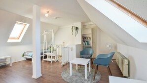 Une chambre spacieuse aménagée en loft, avec une lucarne, un lit blanc, une petite table et une chaise bleue.