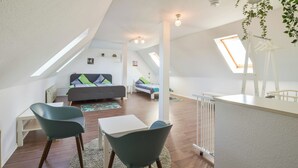 Une chambre de style loft moderne, avec un plafond en pente, des fenêtres de toit, un grand lit, un bureau et deux chaises.