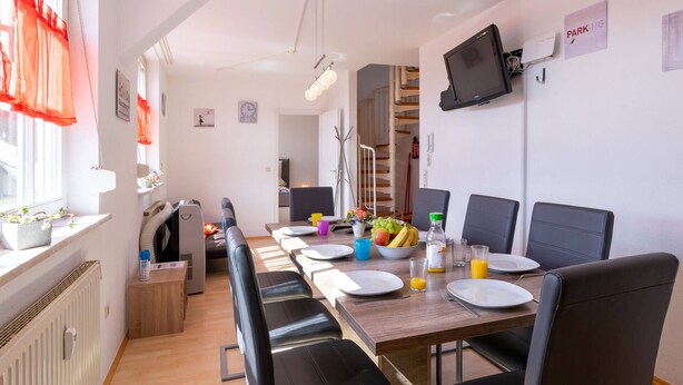 Un espace repas avec une longue table, des chaises noires et un téléviseur fixé au mur.