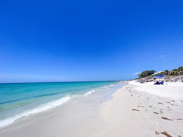 Une plage avec une eau d’un bleu limpide, un rivage sablonneux et quelques parasols.