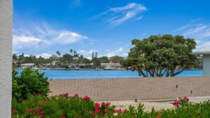 Vista para a orla marítima com piscina, palmeiras e um edifício ao fundo.
