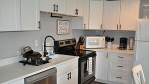 A kitchen with white cabinets, a stove, a microwave, and a coffee maker. - Newly Renovated! CB Condo unit 104 (sleeps up to 8) (Quincy)