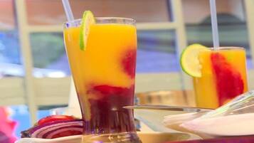 Two tall glasses of fruit juice with lime garnishes, placed on a table with a window view in the background.