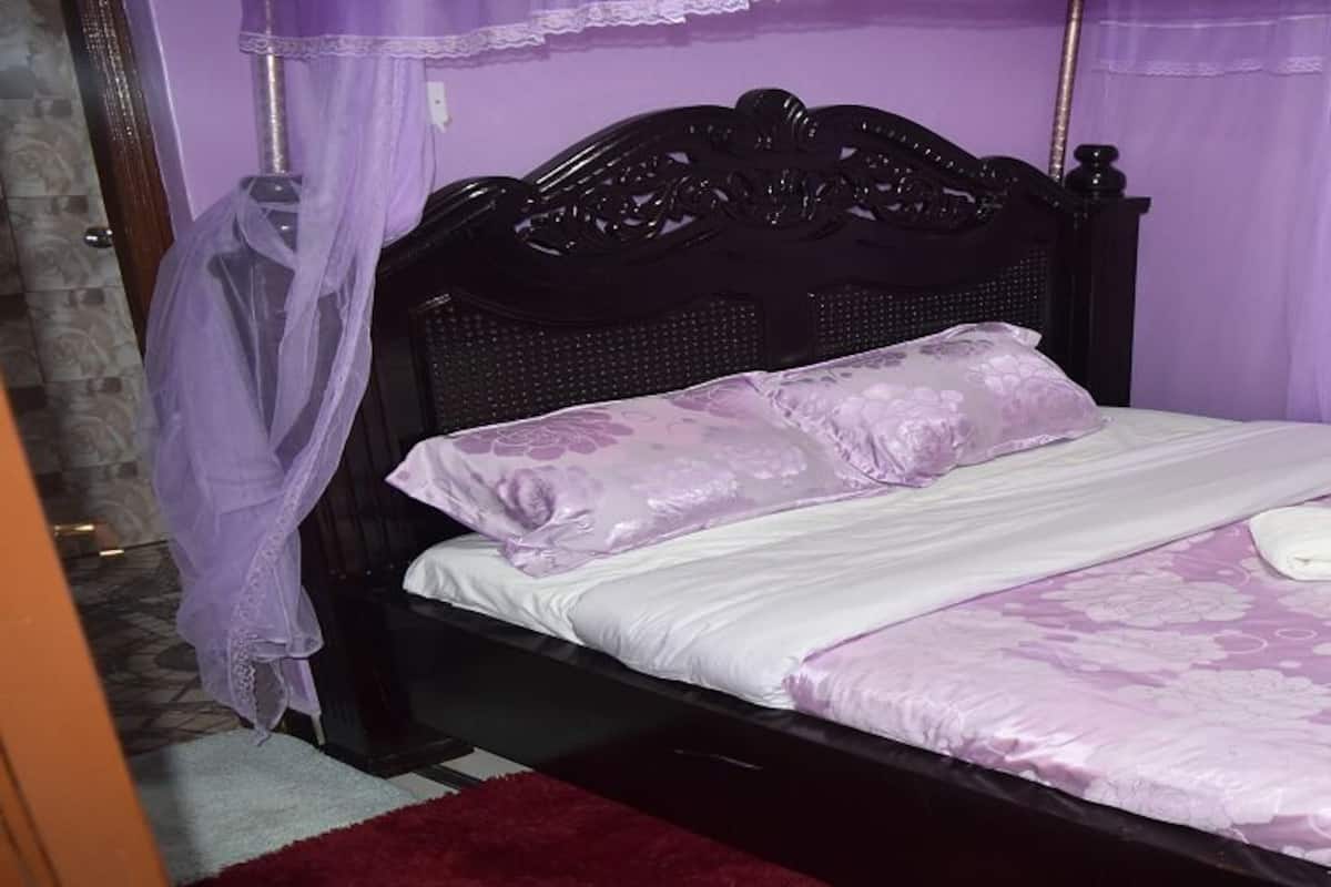 Una cama con colcha floral y toalla blanca, cabecero de madera oscura y pared morada.