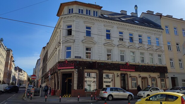 En bygning med en restaurant ved navn 'Elysiom' i stueetagen, præget af klassisk arkitektur med flere vinduer og en tydelig indgang.