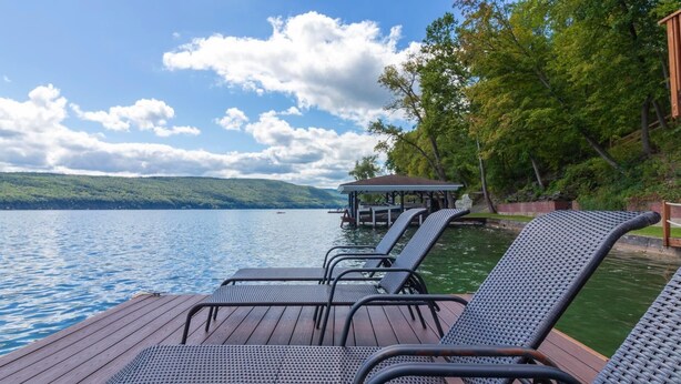 Eine Terrasse mit Liegestühlen mit Blick auf einen See, ein überdachter Sitzbereich und ein bewaldeter Hügel im Hintergrund.