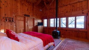Ein Schlafzimmer in einer Holzhütte mit einem Bett, einem Fernseher, einem Kamin und großen Fenstern.
