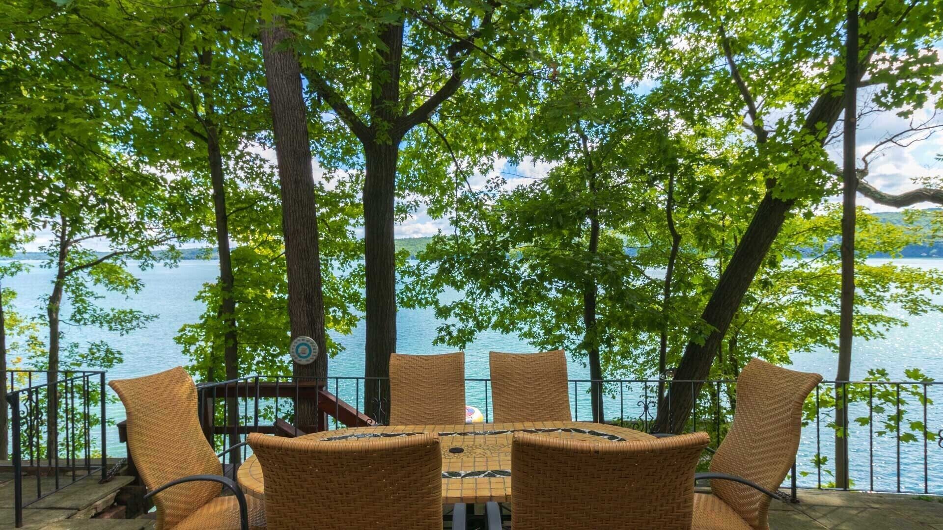 A table and chairs set up on a deck overlooking a lake, surrounded by trees.