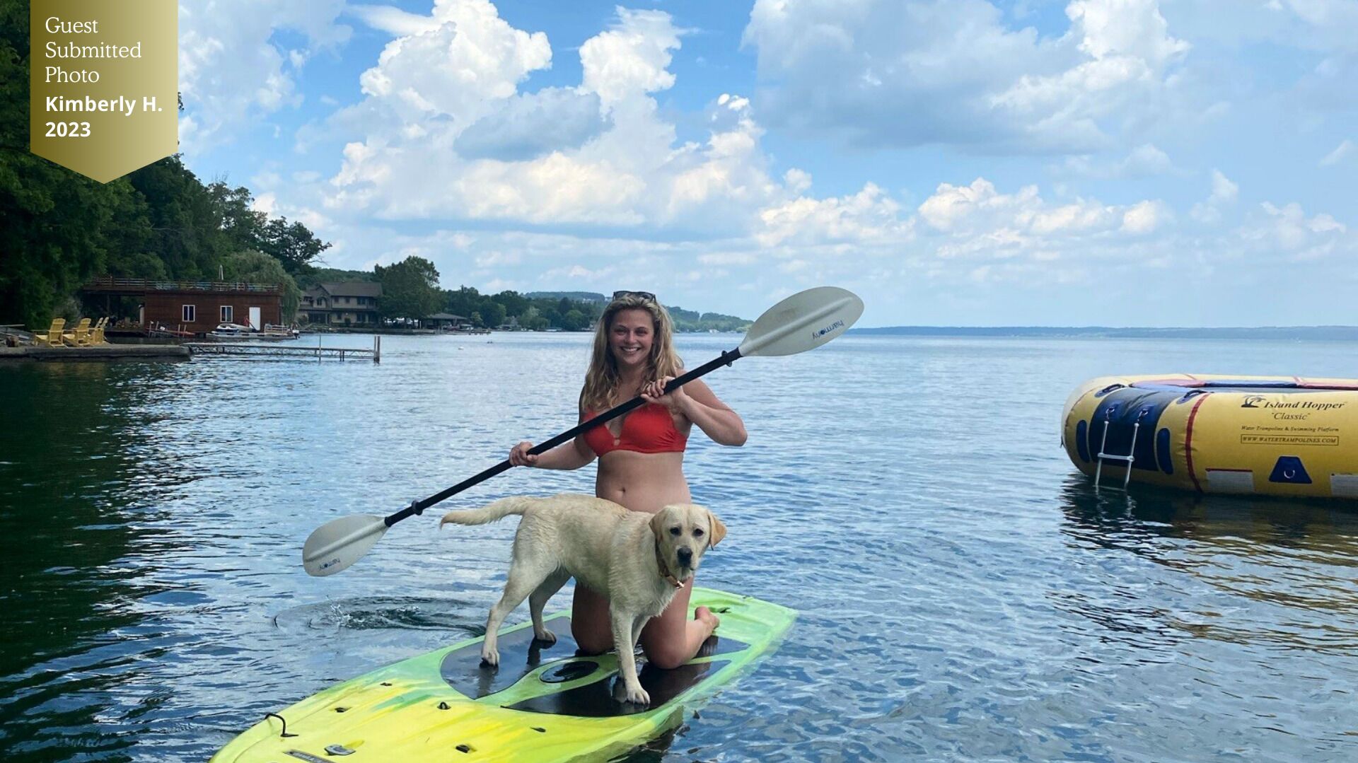 Una persona con traje de baño rojo remar en kayak sobre agua, con un perro en una tabla de remo verde.