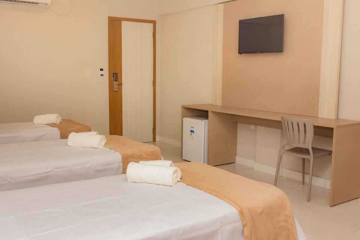 A hotel room with three beds, a desk, a chair, and a television.