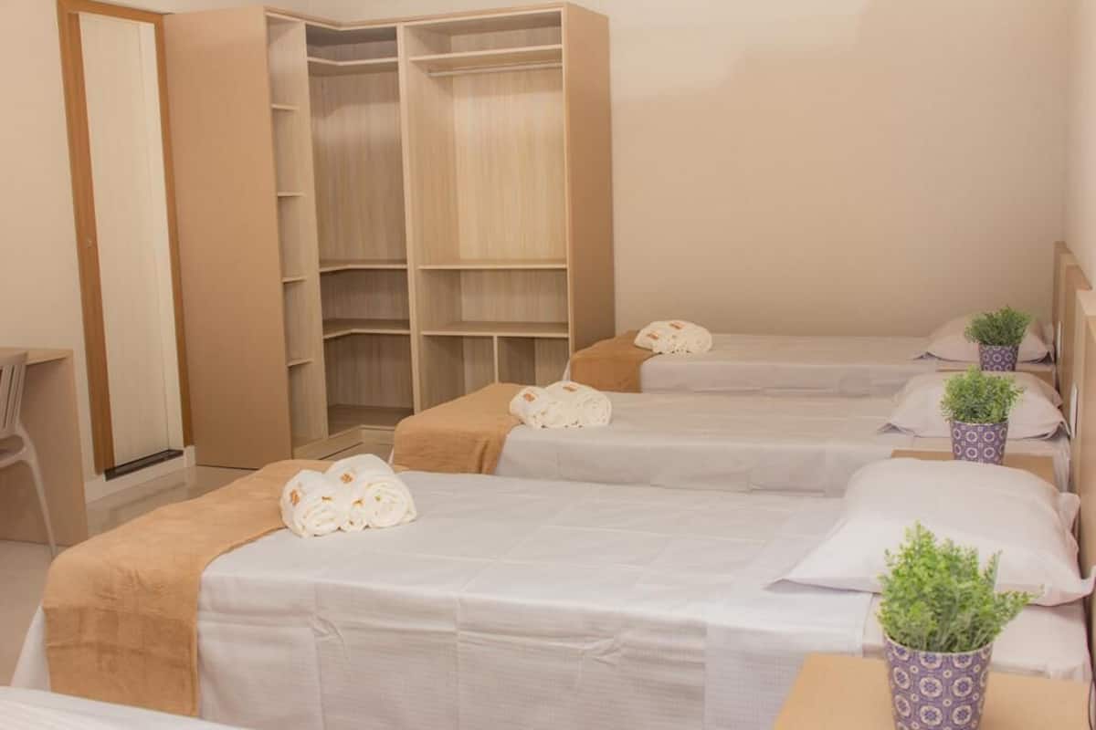 A hotel room with three beds, a large wardrobe, and potted plants.
