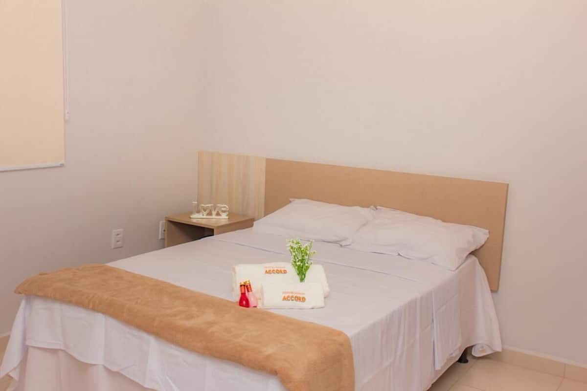 A neatly made bed with white linens, a brown throw blanket, and a small bedside table with a bottle and a decorative item.