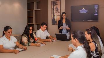 Un salón de conferencias con una pantalla grande mostrando texto, una pizarra y una persona presentando.