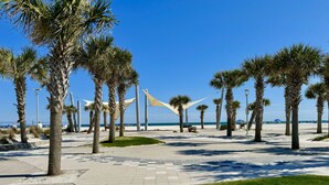 Een verharde promenade met palmbomen en een strand op de achtergrond.