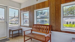 A room with a wooden bench, a small table, and three windows with views of houses. - Hank's Hideaway by Bayley Vacation Rentals (Scarborough)