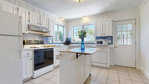 Une cuisine avec des meubles blancs, un îlot central, un four à micro-ondes et une cuisinière.