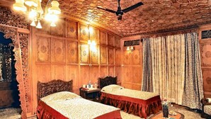 A traditional room with two beds, ornate wooden paneling, a ceiling fan, and a small table with a vase. - Meena Group houseboats (Srinagar)