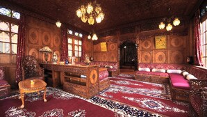 A richly decorated room with ornate wooden furniture, a large chandelier, and intricate wall designs. - Meena Group houseboats (Srinagar)
