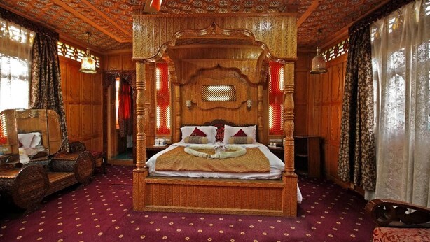 A traditional wooden four-poster bed with a canopy, a red patterned carpet, and a wooden floor. - Meena Group houseboats (Srinagar)