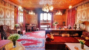 A traditional room with ornate wooden ceilings, patterned walls, and a central seating area with a sofa and a table. - Meena Group houseboats (Srinagar)