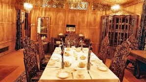 A formal dining room with a long table set for a meal, ornate wooden chairs, and a chandelier. - Meena Group houseboats (Srinagar)