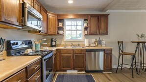 A kitchen with wooden cabinets, stainless steel appliances, a window, and a bar stool. - 4BR Ranch • 1 Mile to Downtown Cartersville (Cartersville)