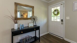 A hallway with a black console table, a mirror, a decorative windmill, and a door with a wreath. - 4BR Ranch • 1 Mile to Downtown Cartersville (Cartersville)